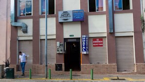 A building with a Hostal sign, a closed shutter door, and a person standing by the entrance. - Hostal Downtown Quito (Quito)