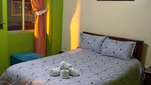 A bedroom with a bed, a window with curtains, a bedside table, and a painting on the wall. - Hostal Downtown Quito (Quito)