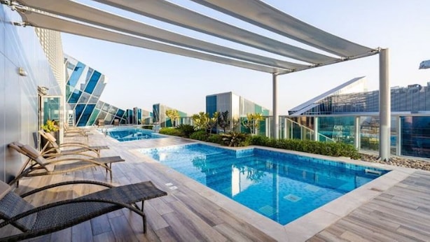Una piscina en la azotea con sillones de descanso, una pérgola y edificios modernos al fondo.