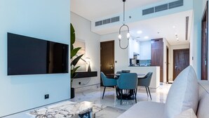 Una sala moderna con televisor de pantalla plana, un comedor con sillas azules y una cocina al fondo.