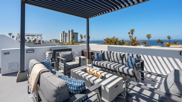 Eine Dachterrasse mit Sitzgelegenheiten im Freien, einem Feuerkorb und Blick auf das Meer und die Stadt.
