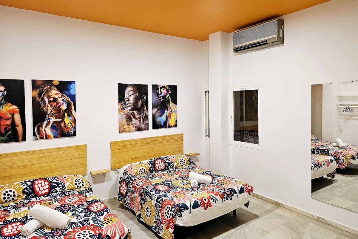 A hotel room with two beds, a large mirror, and three paintings on the wall.