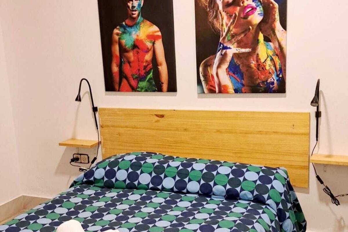 A bedroom with a bed, two wall-mounted lamps, and two paintings.