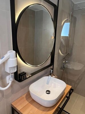 Une salle de bain moderne avec un miroir rond, un lavabo blanc et un sèche-cheveux fixé au mur.