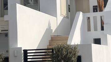 Ein modernes Gebäude mit einem schwarzen Tor, einer Treppe und einem Schild mit der Aufschrift 'Thelos Santorini'.