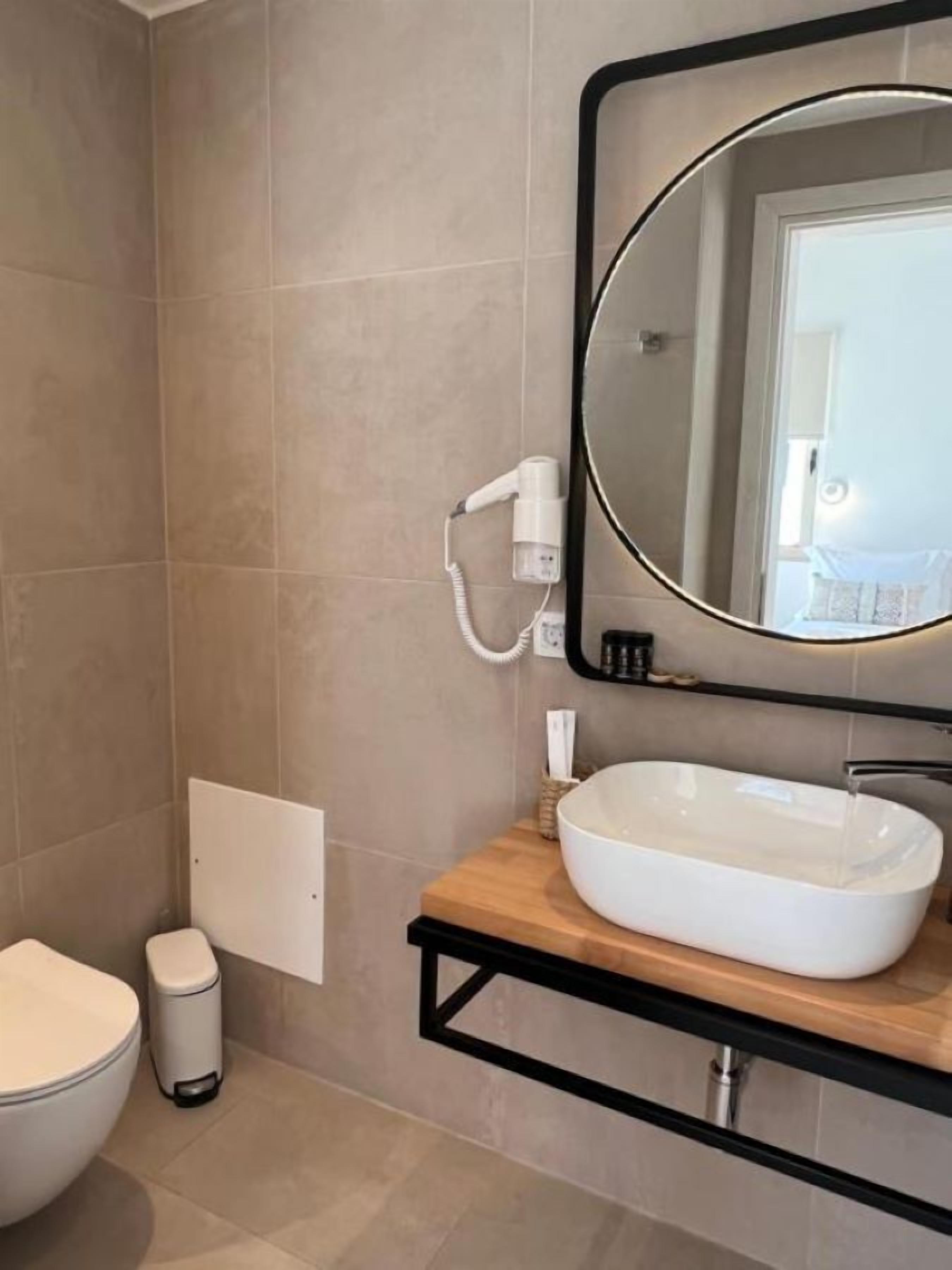 A modern bathroom with a large oval mirror, a white sink, and a handheld hair dryer mounted on the wall.