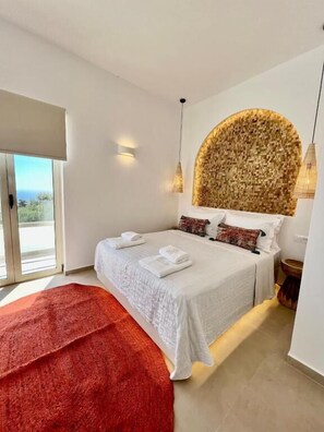 Une chambre à coucher moderne avec un grand lit, un plaid rouge et une tête de lit originale en tissu tissé.