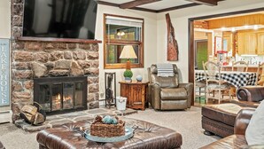 A cozy living room with a stone fireplace, leather furniture, and a television mounted on the wall. - Ranch on Greenwood: Hot tub , fire pits, kayaks, Rafts, Bikes (Lake Harmony)