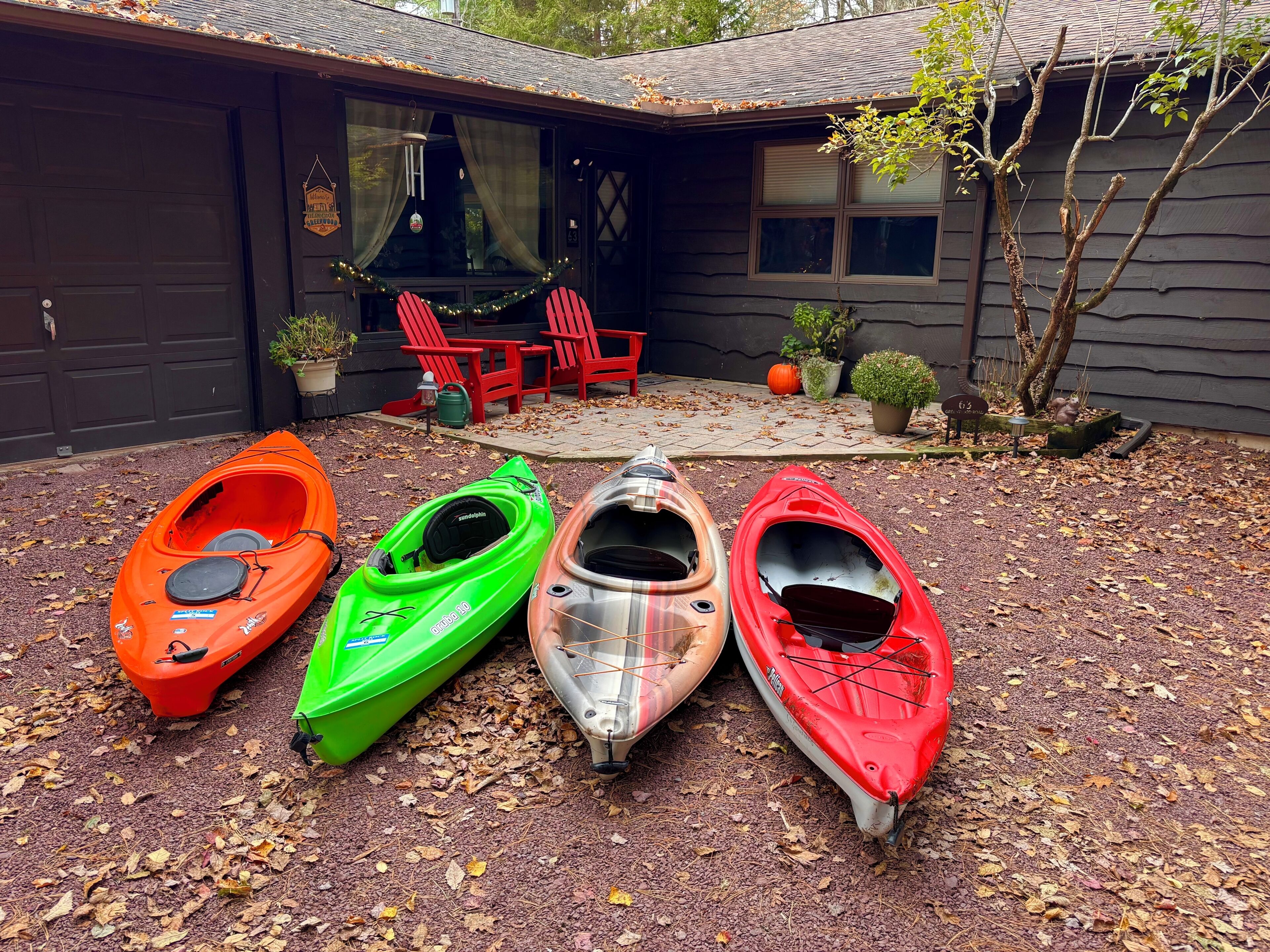 Quatre kayaks étaient alignés devant une maison dotée d’un garage, d’une terrasse avec des chaises rouges et de plantes en pot.