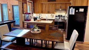 A kitchen with wooden cabinets, a stainless steel refrigerator, a coffee machine, and a dining table with chairs. - Ranch on Greenwood: Hot tub , fire pits, kayaks, Rafts, Bikes (Lake Harmony)