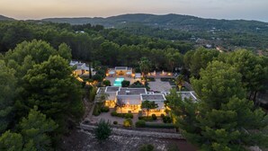Una villa moderna con piscina, rodeada de bosque denso y colinas.