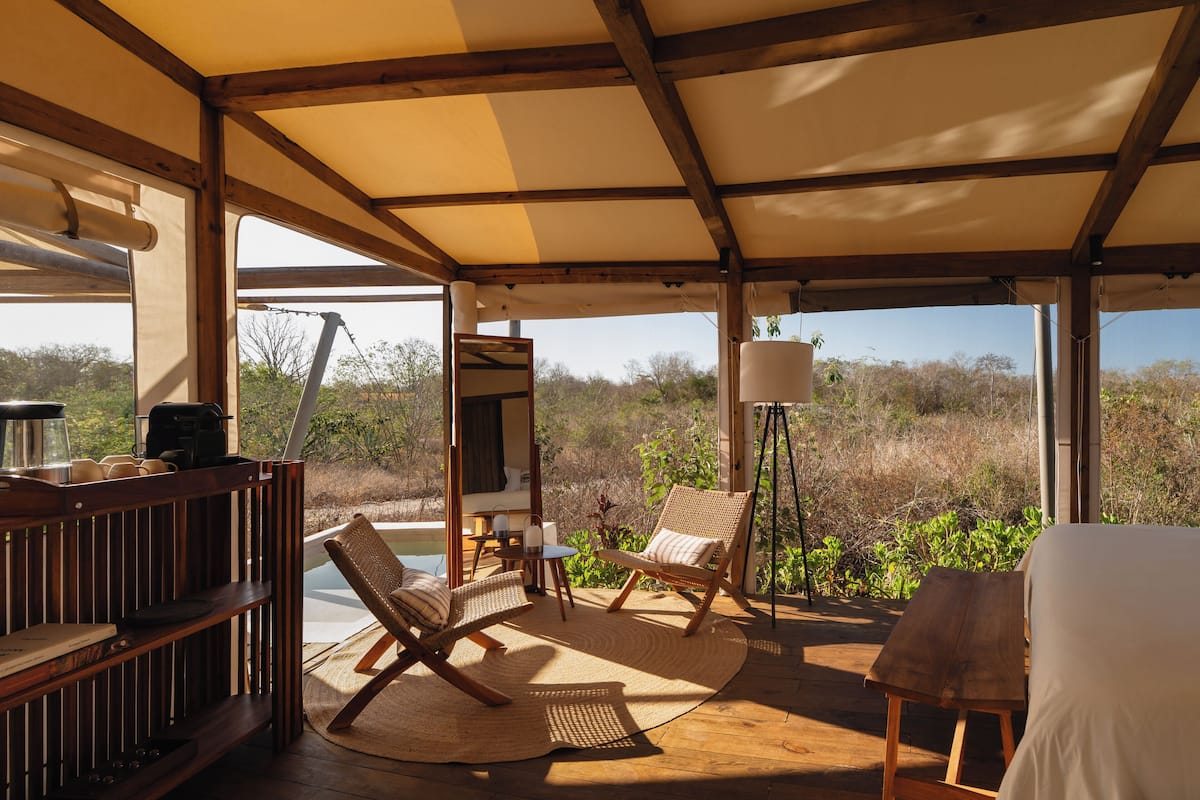A covered outdoor seating area with wooden furniture, a table, and a view of the surrounding landscape.