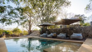 A swimming pool with a stone wall and trees in the background. There are lounge chairs and umbrellas. - Viatura Hacienda Xtojil, Yucatan, Merida, with Optional All Inclusive (Timucuy)