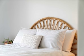 Ein Bett mit einem gewobenen Kopfteil, zwei Kissen und einer weißen Bettdecke.