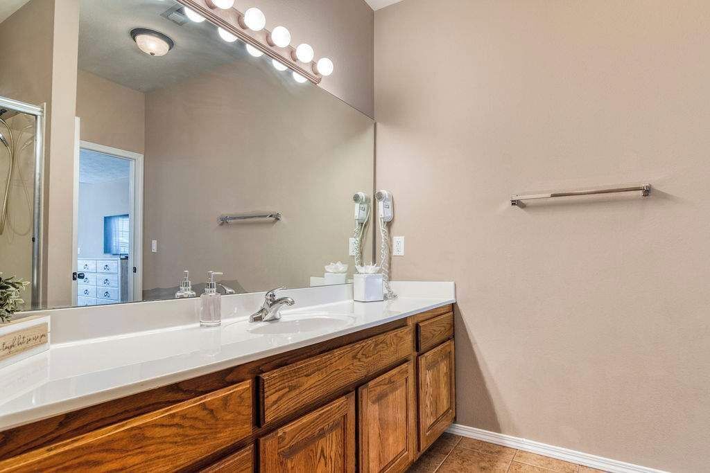 A bathroom with a large mirror, vanity with a sink, two hair dryers, and a towel rack.