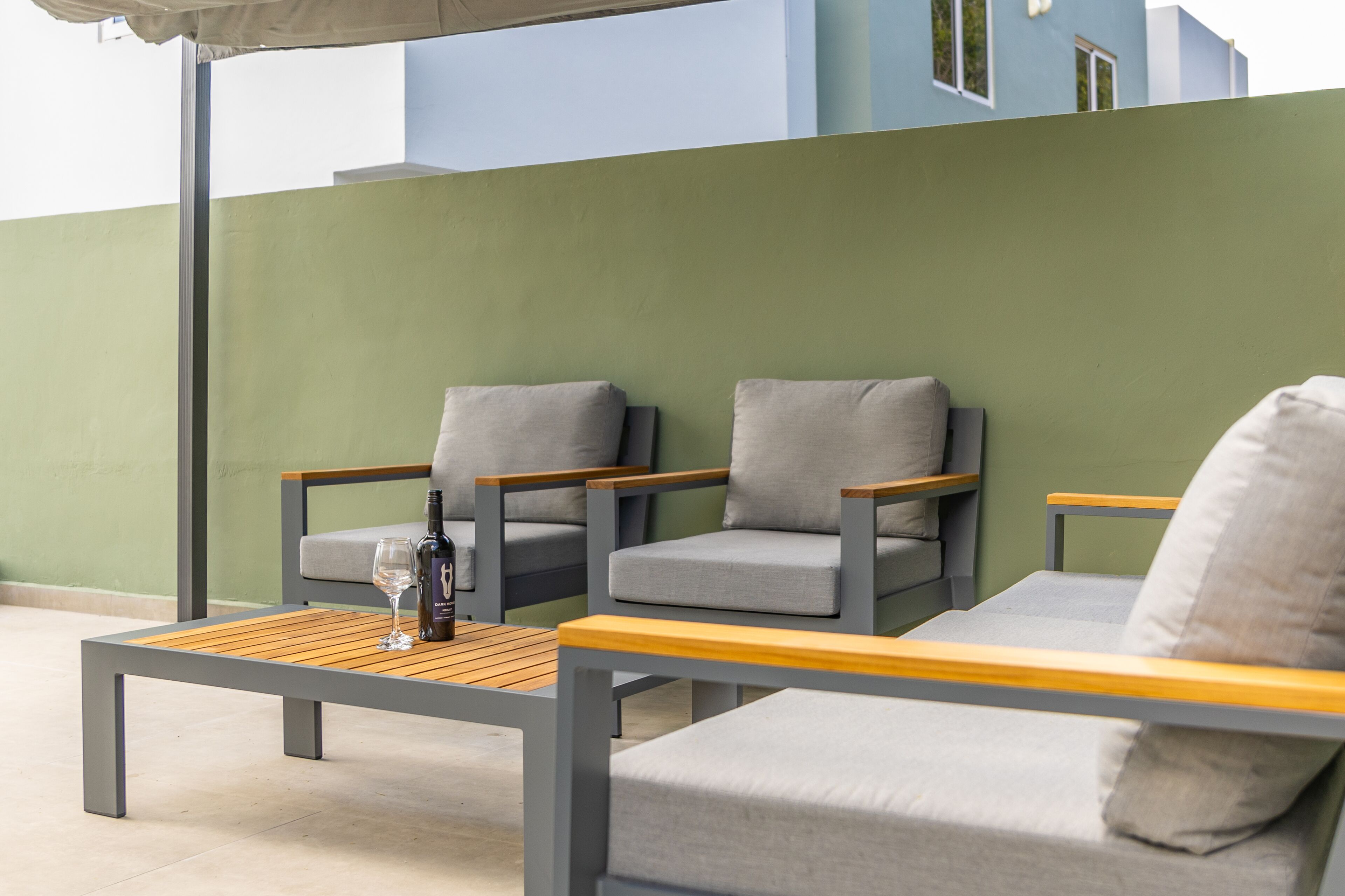 A patio area with two grey upholstered chairs, a wooden table, and a bottle of wine.