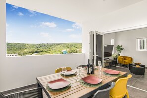 A dining area with a table set for four, a view of a green landscape, and a yellow chair. - Modern 3-bed Apartment in Papaya Resort Curacao (Grote Berg)