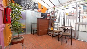 A reception area with a fire extinguisher, a potted plant, a wooden cabinet, and a glass door with a sign. - Hostal Whipala (Quito)