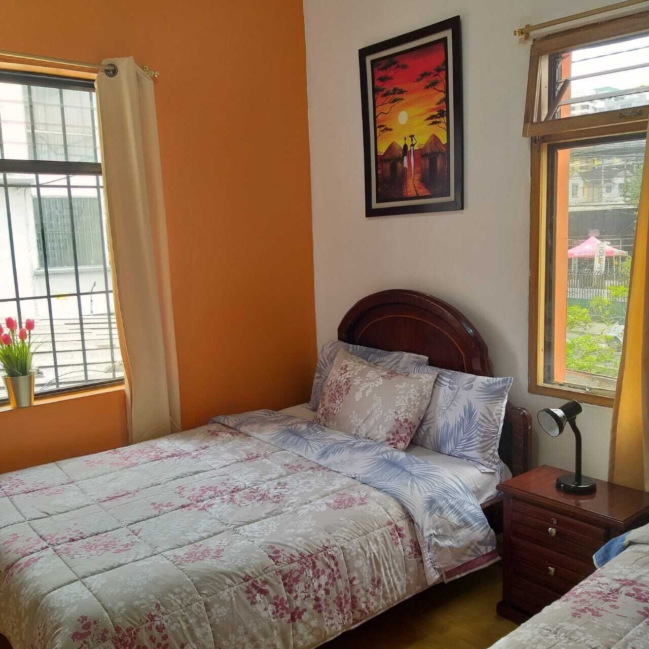 A bedroom with a bed, a nightstand, a window with a view, and a painting on the wall.