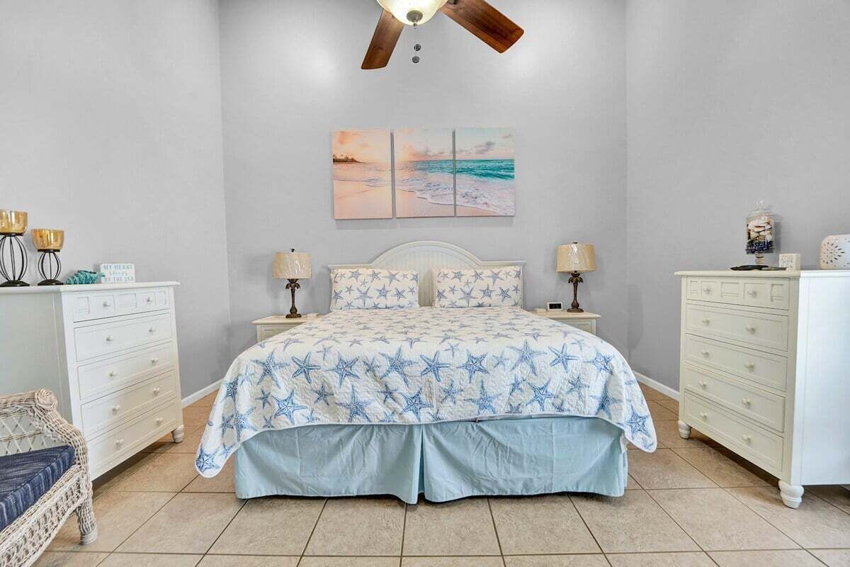 Ein Schlafzimmer mit einem Bett, zwei Nachttischen, einer Kommode, einem Sessel und einem Deckenventilator.