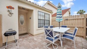 Eine Terrasse mit einem weißen Tisch, blauen Stühlen, einem Grill und einem Holzzaun.