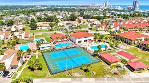An aerial view of a residential area with multiple buildings, a large tennis court, and a swimming pool.