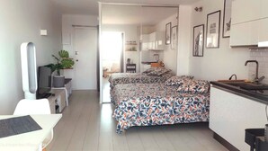 Un dormitorio moderno y bien iluminado, con una cama grande, un escritorio con silla, un televisor y una planta.