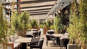 An outdoor cafe with tables and chairs, surrounded by greenery and modern architecture. - Hyatt Regency London Stratford (London)