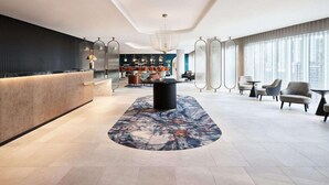 A modern hotel lobby with a reception desk, seating area, and large windows offering a city view. - Hyatt Regency London Stratford (London)