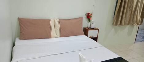 Una cama bien hecha con ropa de cama blanca y beige, una mesita de noche con un jarrón de flores y una alfombra azul estampada.