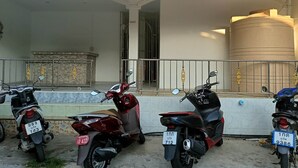 A covered parking area with four motorcycles parked in front of a building with a large water tank. - Kata S.T House 2 (Karon)
