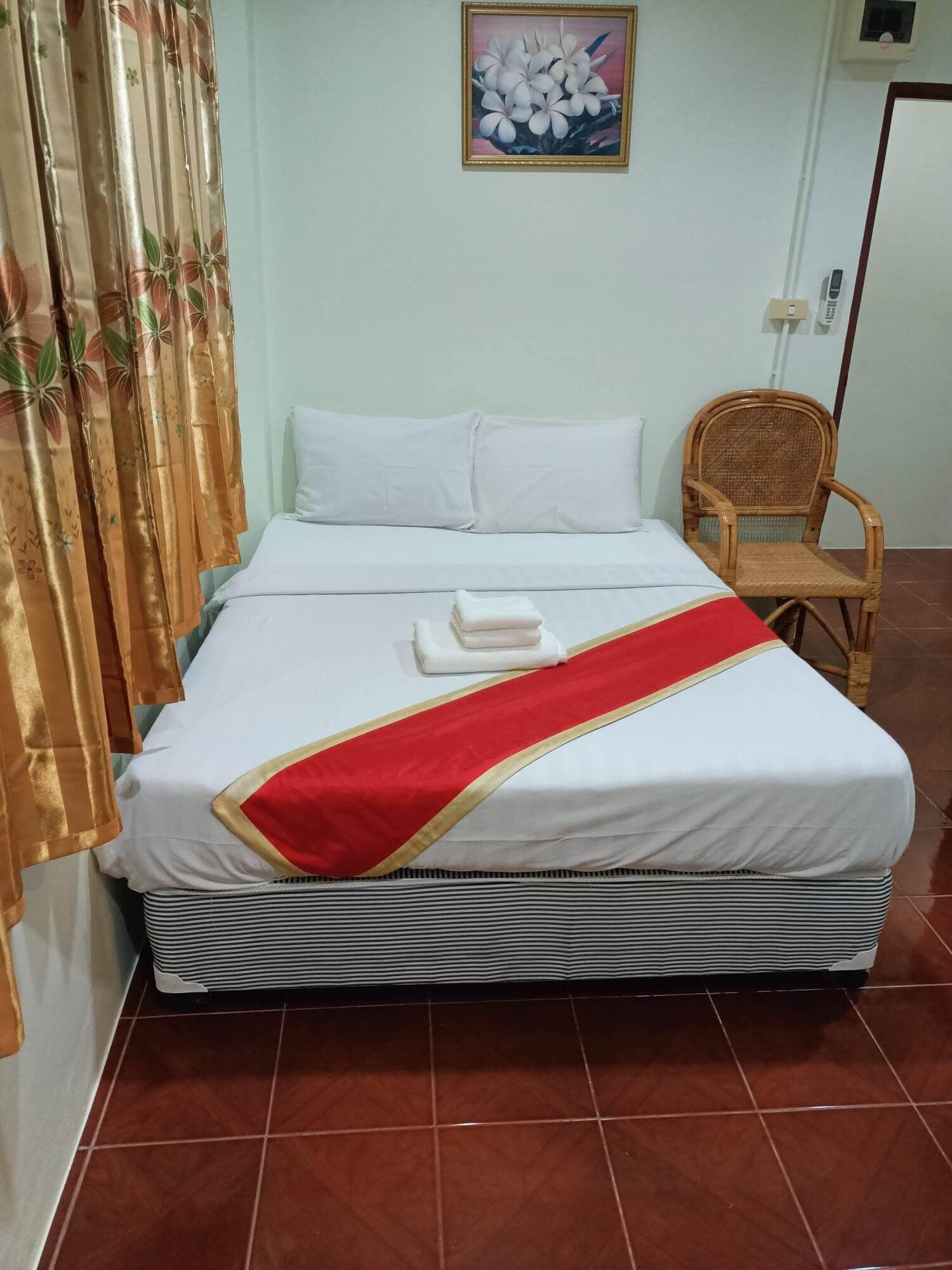 A neatly made bed with white linens, a red and gold bed runner, and a white pillow.
