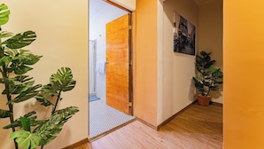 Un pasillo con suelo de madera, una planta de monstera en maceta y una puerta que da a otra habitación.