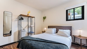 Habitación de hotel con una cama grande, un armario, un espejo, una mesita de noche y una ventana con vistas a árboles.
