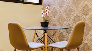 Un comedor con mesa de vidrio, dos sillas amarillas y una orquídea en maceta.