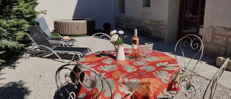 Una mesa redonda con mantel floral rojo, rodeada de sillas de metal. Hay dos botellas y dos vasos sobre la mesa.