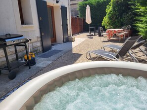 Un jacuzzi en un patio trasero con área de terraza, mobiliario exterior y una parrilla.