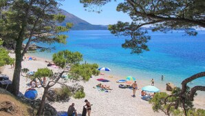 Ein Strand mit klarem, blauem Wasser, badenden Menschen und Sonnenschirmen.