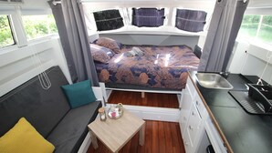 A compact RV interior with a bed, kitchenette, and seating area.