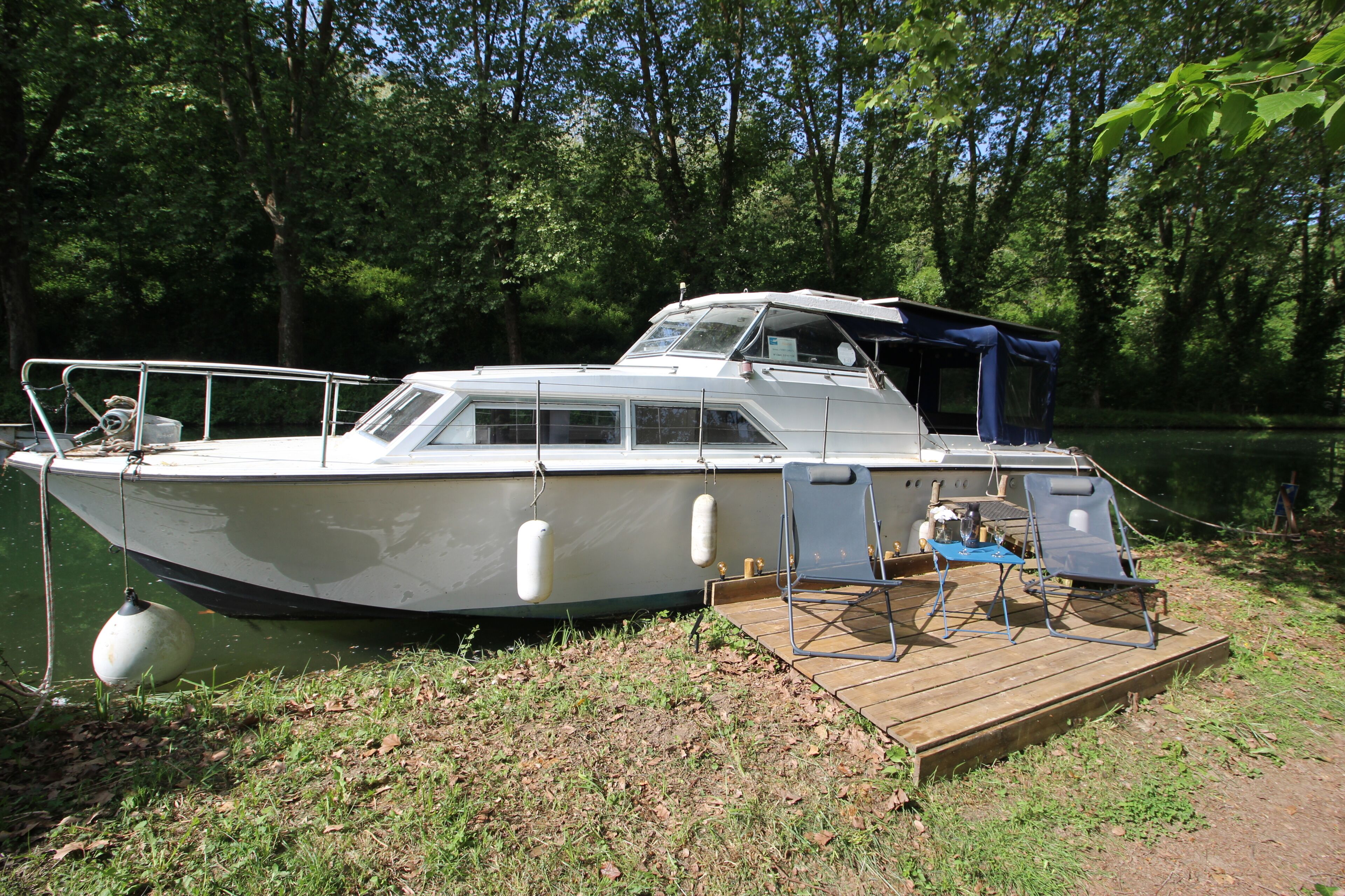 Un bateau était amarré à un quai en bois, doté d’une zone abritée et de deux chaises.