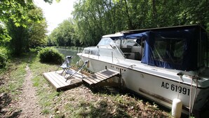 A boat docked at a riverside with a wooden deck and a covered seating area.