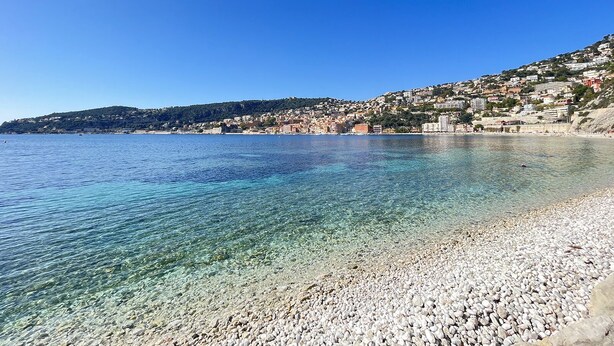 Un poble costaner amb aigües cristal·lines, platja de petits còdols i edificis alçada sobre un turó.