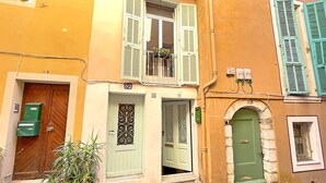 Un carrer estret amb edificis d'arquitectura tradicional, incloent una porta verda i un balcó amb plantes en testos.
