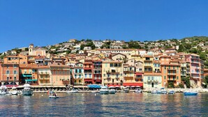 Un poble costaner amb edificis de colors, vaixells amarrats al costat i un cel blau i clar.