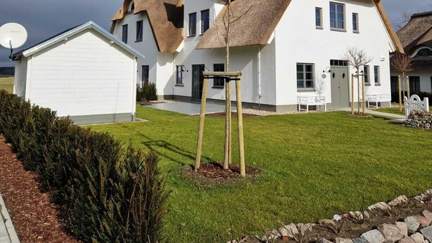 A modern house with a white exterior, a thatched roof, and a satellite dish.