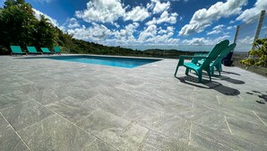 A swimming pool with a tiled deck and a few green chairs. - Villa sea view from 3 to 11 people (Rivière-Salée)