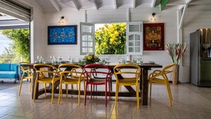 A dining area with a table set for six, surrounded by yellow and red chairs, with a view of greenery outside. - Villa sea view from 3 to 11 people (Rivière-Salée)