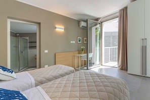 A hotel room with two beds, a bathroom, a balcony, and a dining area.