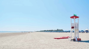 A beach with a lifeguard tower, a red kayak, and beach umbrellas. - Villa with all comfort (Albarella)