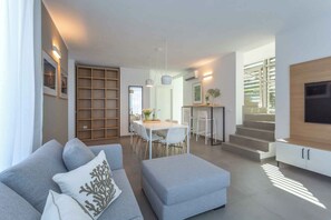 A modern living room with a sofa, ottoman, and a dining area with chairs and a table. - Villa with all comfort (Albarella)